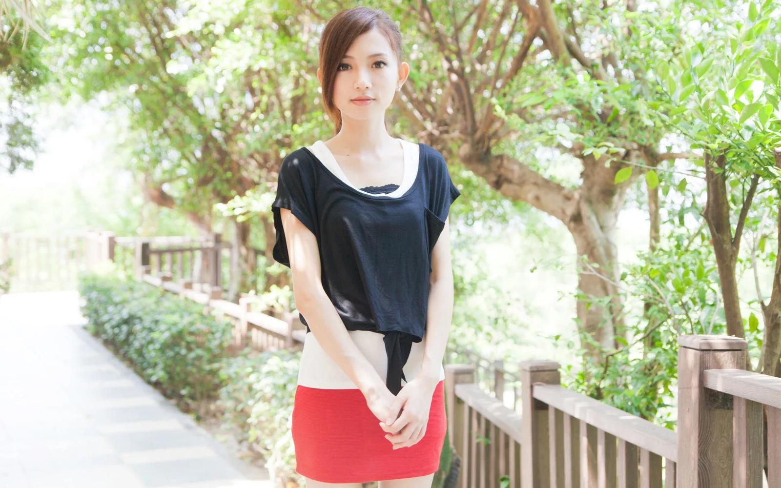 一名成年女性站在绿树环绕的木栈道旁。