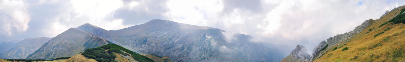 雲に包まれた山々や稜線、金色の斜面が広がるパノラマ風景です。