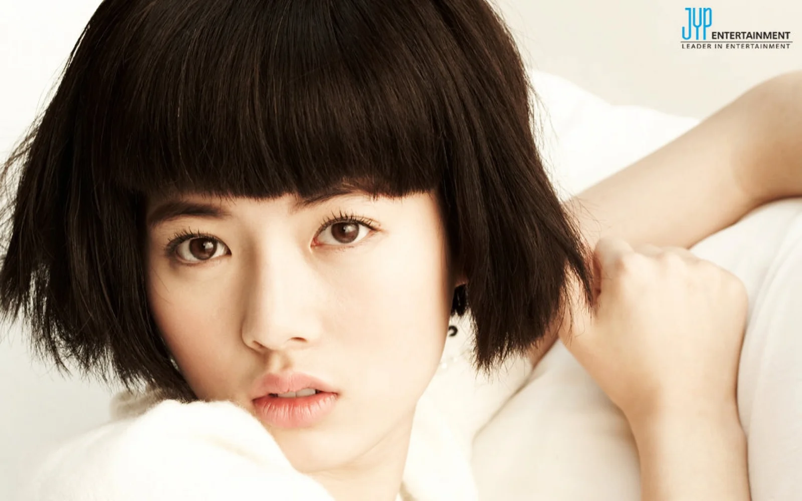 短いボブヘアの成人女性が、明るくシンプルな背景の前でカメラを見つめています。