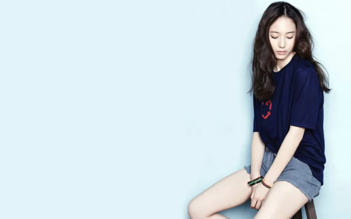 一名长发女子穿着深蓝色上衣和灰色短裤坐在浅蓝色背景前。