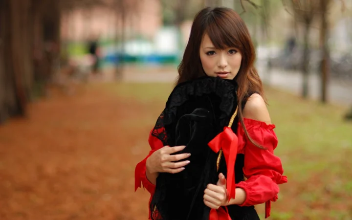 一名成年女子在户外穿着红色上衣，手持黑色布料。