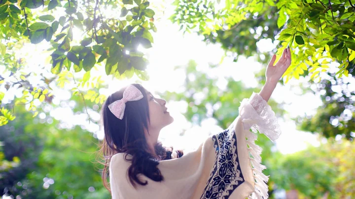 一名女子在阳光洒落的树荫下伸手触碰枝叶。