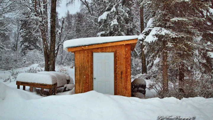 积雪覆盖的森林中，一座木制小屋被厚厚的白雪包围。