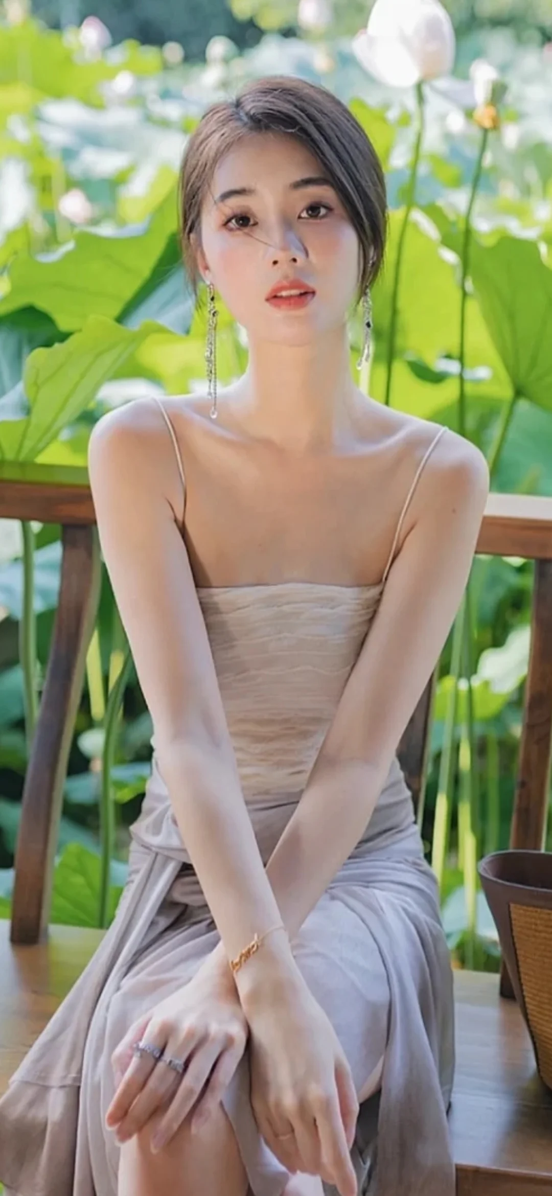 밝은 색상의 원피스를 입은 성인 여성이 연잎 곁에 앉아 카메라를 바라보고 있습니다.
