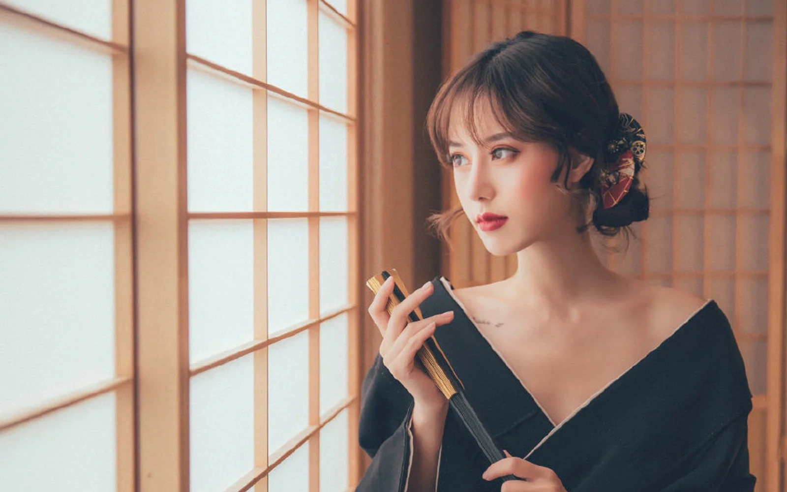 一位佩戴发饰的女性身着黑色服装，站在木格窗前望向一侧。