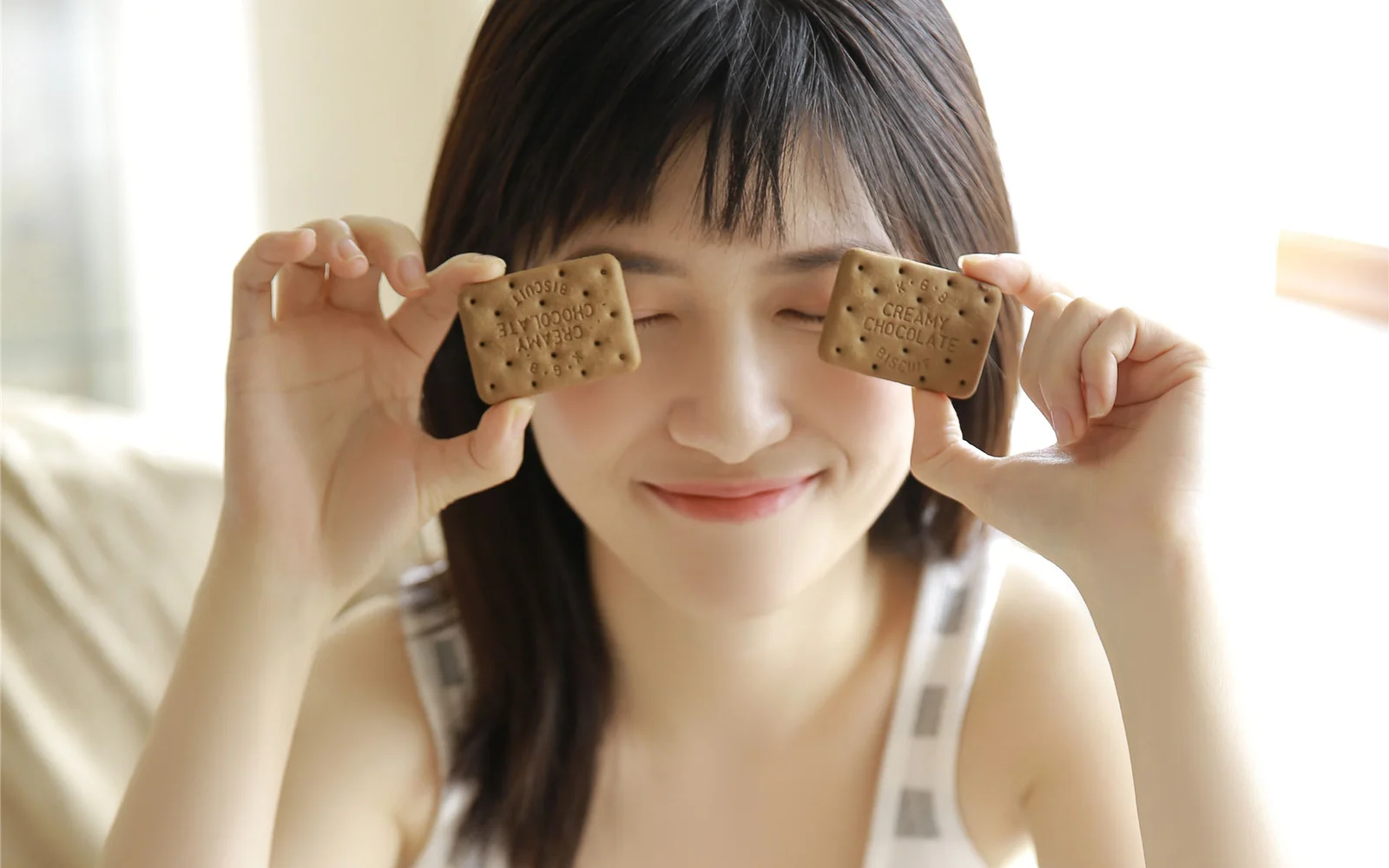 一名微笑的年轻女子拿着两块饼干遮住眼睛。