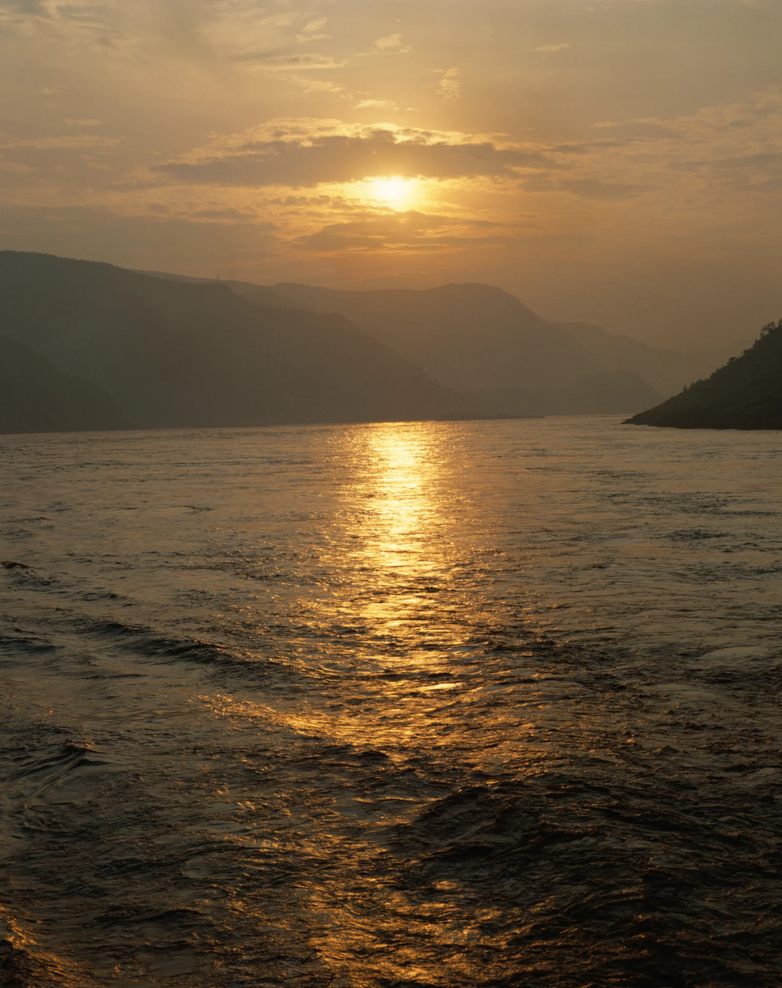 夕日が湖面を照らし、遠くの山々が黄金色の霞に包まれている。