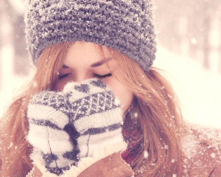 一名戴着针织帽和围巾的成年女性闭眼站在飘雪中。