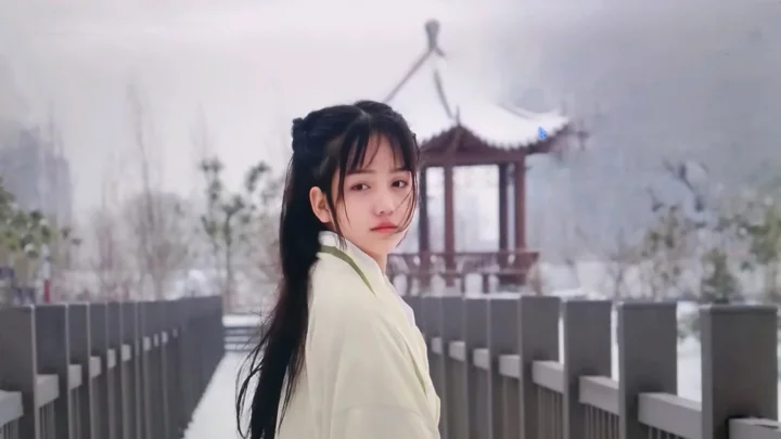 一名长发女子站在桥上回头望向镜头，背景可见朦胧的亭子和树木。