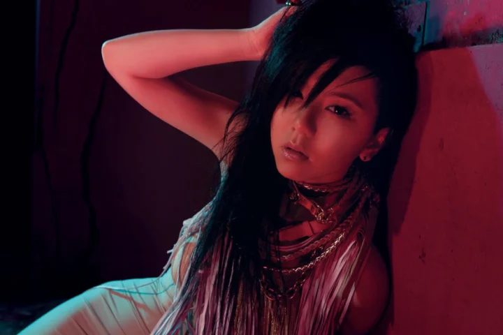 一名女性在红色和蓝绿色光影交织的昏暗环境中靠墙摆姿势。