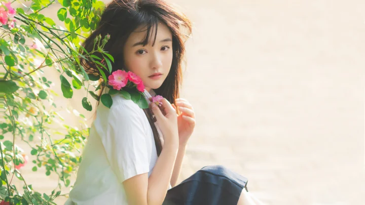 一位年轻女性在绿叶与粉色花朵间轻抚发丝。