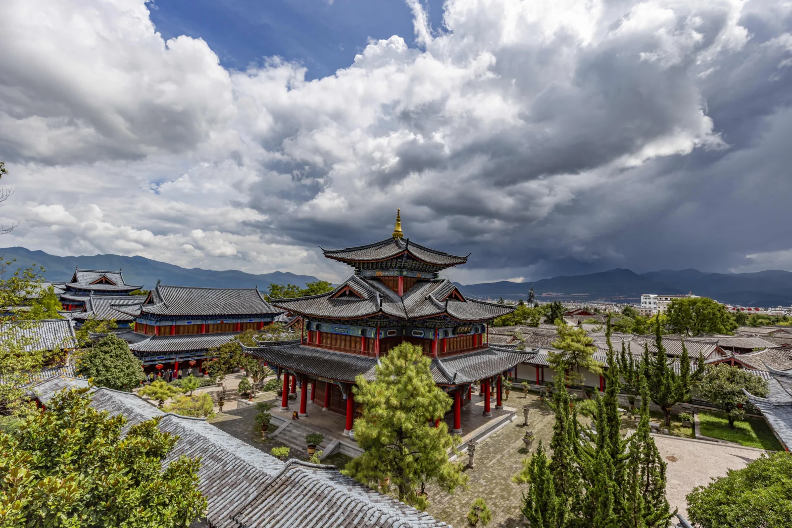 山々に囲まれた中国の伝統建築群の上に、暗い雲と白い雲が幾重にも広がっています。