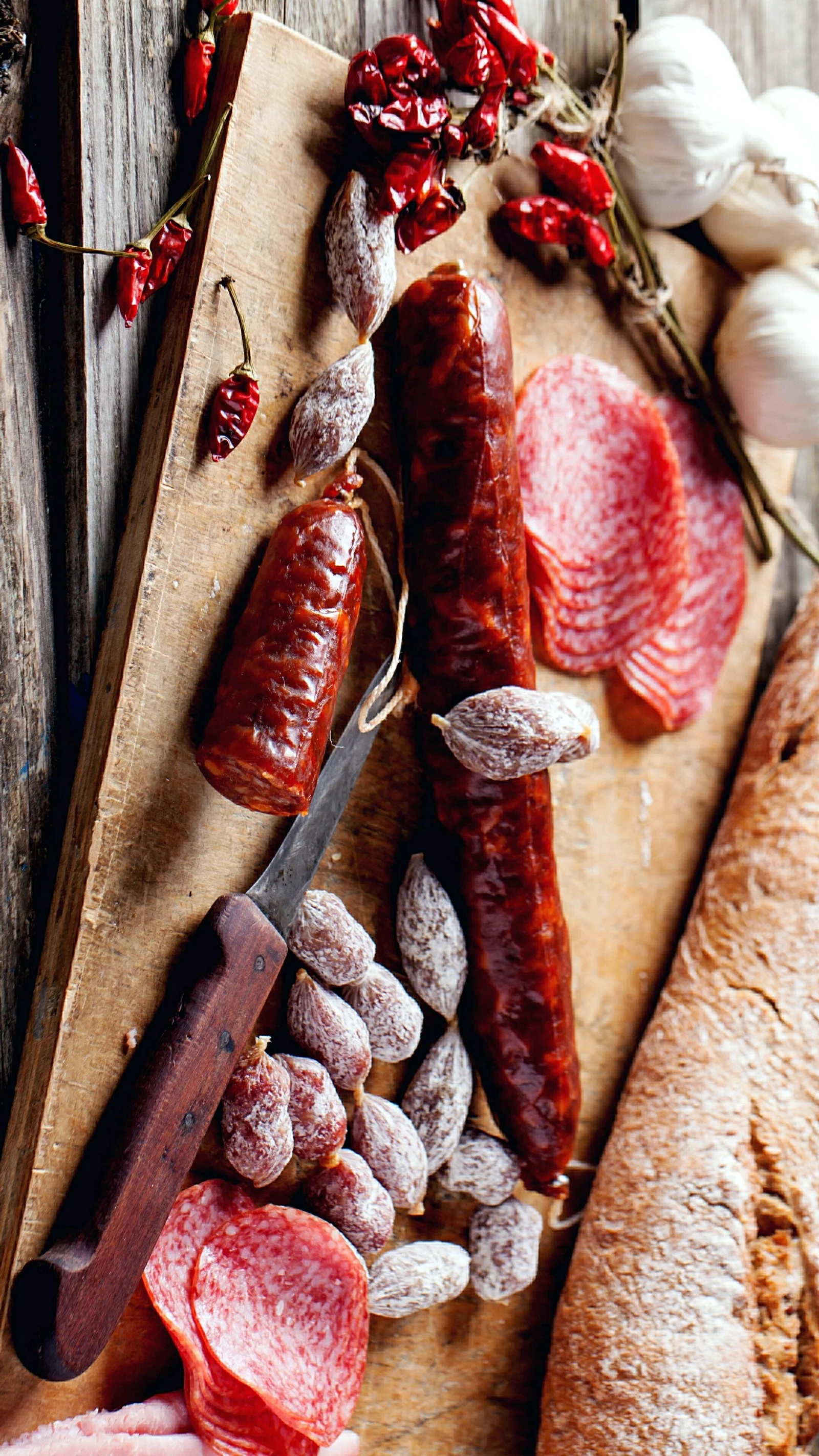 木板上摆放着香肠、切片腌肉、干肉、辣椒、大蒜和面包。
