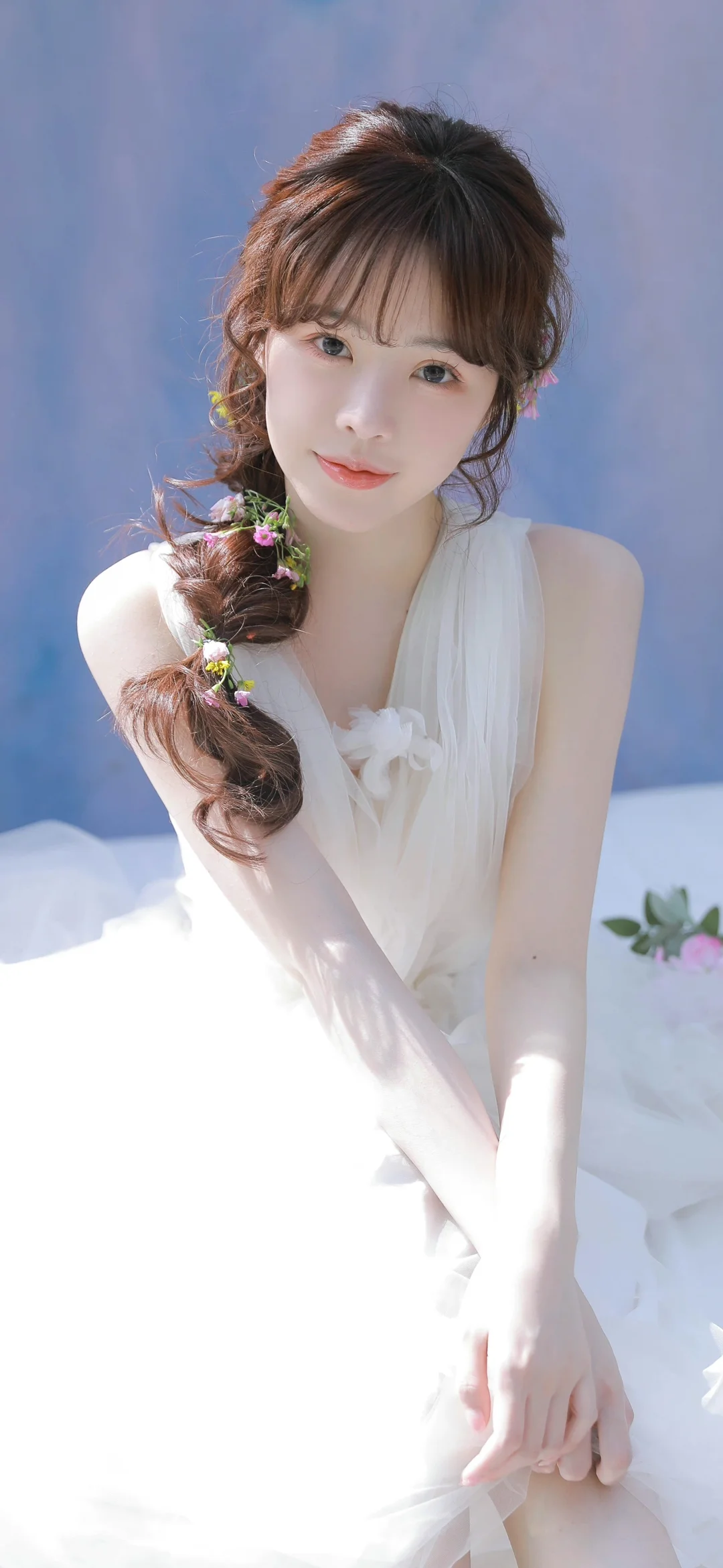 一位留着编发、身穿白色连衣裙的女性坐在柔和的蓝色背景前。