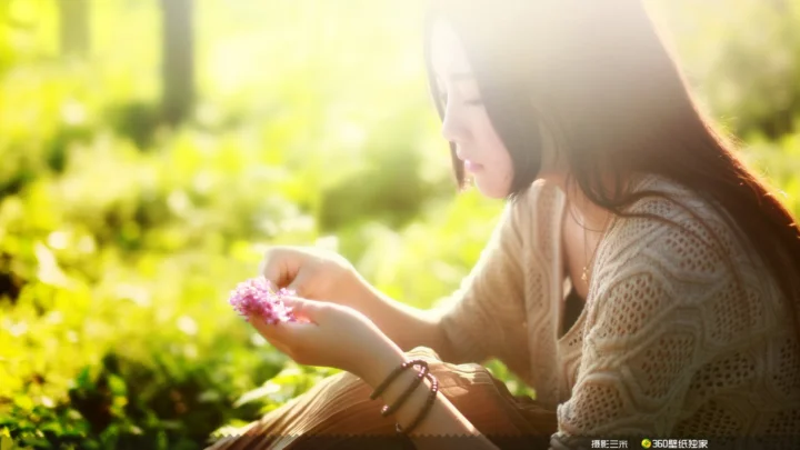 明るい日差しの屋外で、女性が小さな花を手にしている。