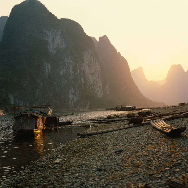 夕阳映照着山间河流、岩岸与停泊的小船。
