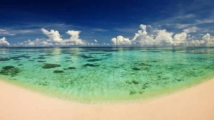 清澈的绿松石色海水延伸至浅色沙滩，远处海平面上方飘着蓬松的白云。