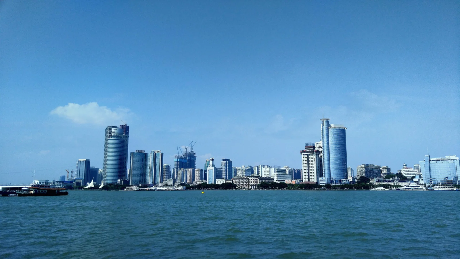 蓝天下，海面前方是一座由高层建筑组成的现代城市天际线。