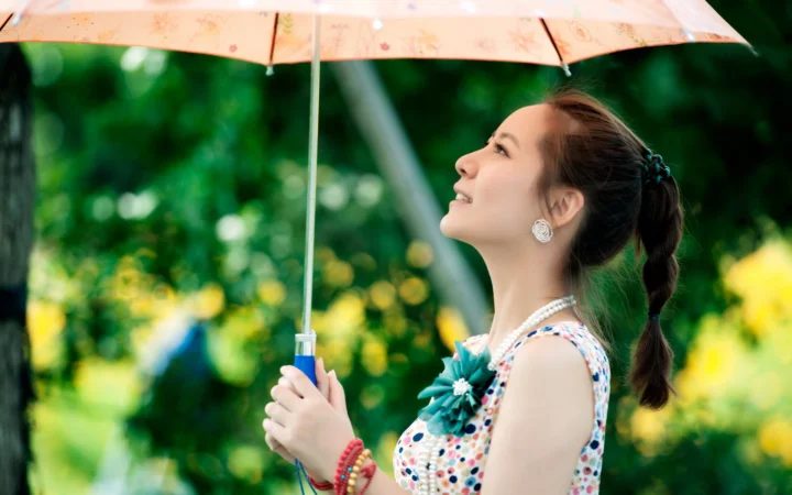 一名成年女子在绿色户外背景前撑着浅色雨伞。