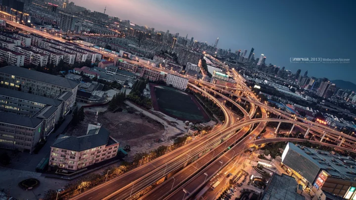俯瞰夜幕下灯光交织的城市建筑群与多层立交道路。