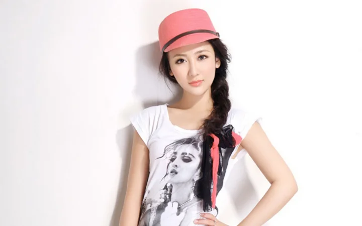 一名戴粉色帽子、留着侧编发的女性站在白色背景前摆姿势。