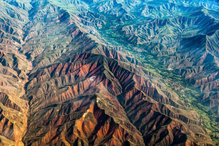 航拍视角展现了层叠起伏的山脉、深邃沟壑和山间绿色谷地。