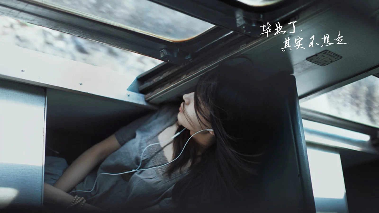 一名成年女性侧身坐在车厢内，头发垂落在肩旁，车顶天窗和窗外景色清晰可见。