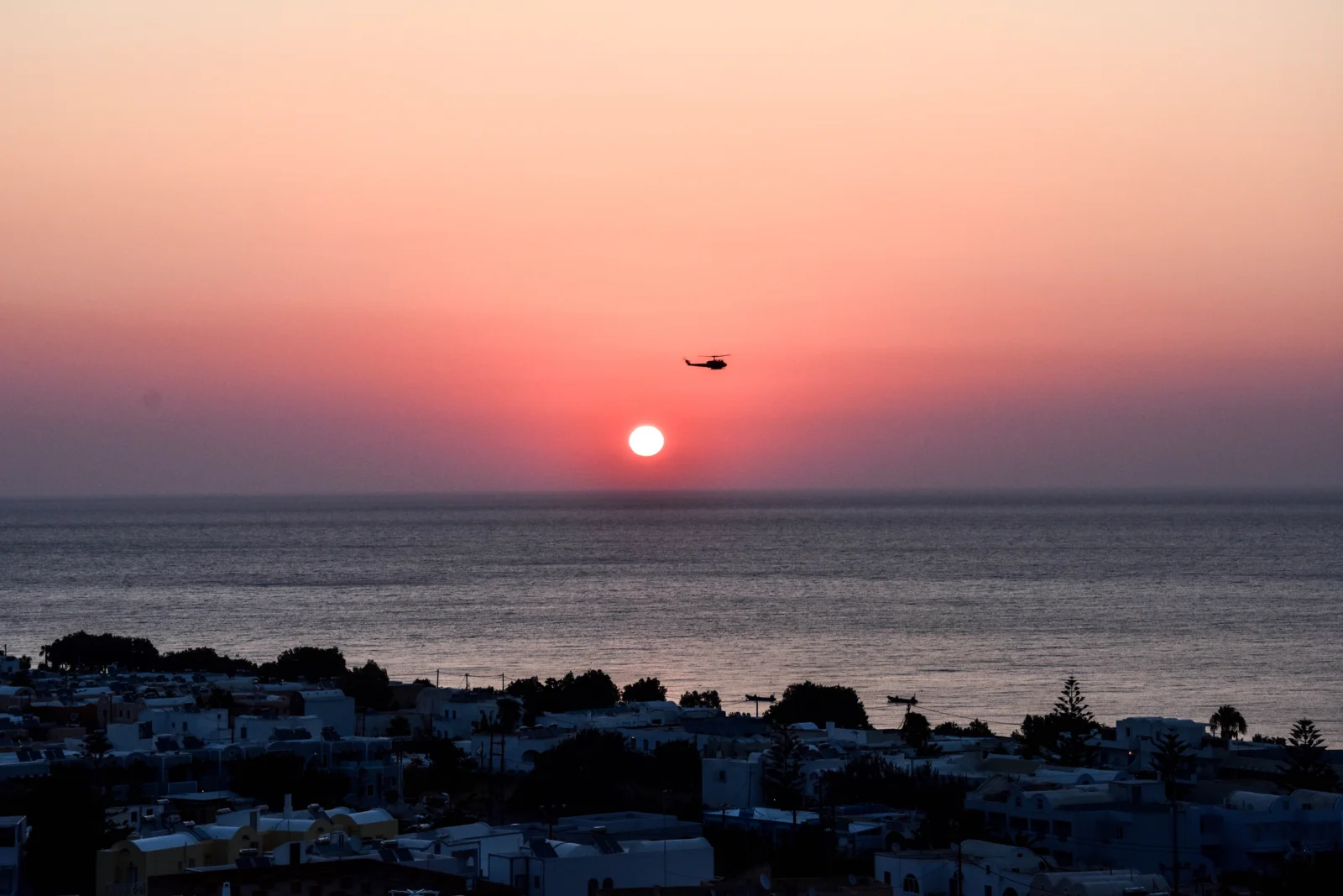 夕阳沉入海平面上方，映照着宁静海面和前景中的海岸小镇。
