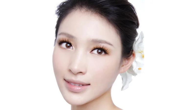一位成年女性在白色背景前面向镜头微笑，耳后可见白色花朵。