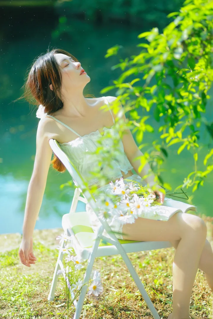 一名身穿白裙的女子坐在户外折叠椅上，周围是绿叶和雏菊。