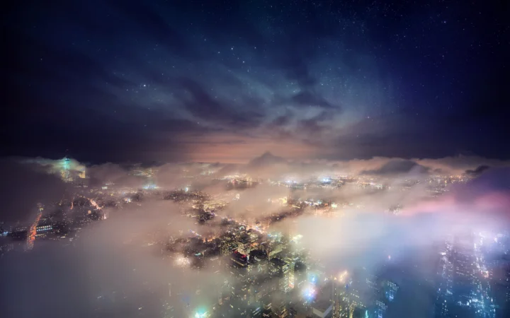 夜幕下的城市灯光在云雾中铺展，远处天空可见星光。