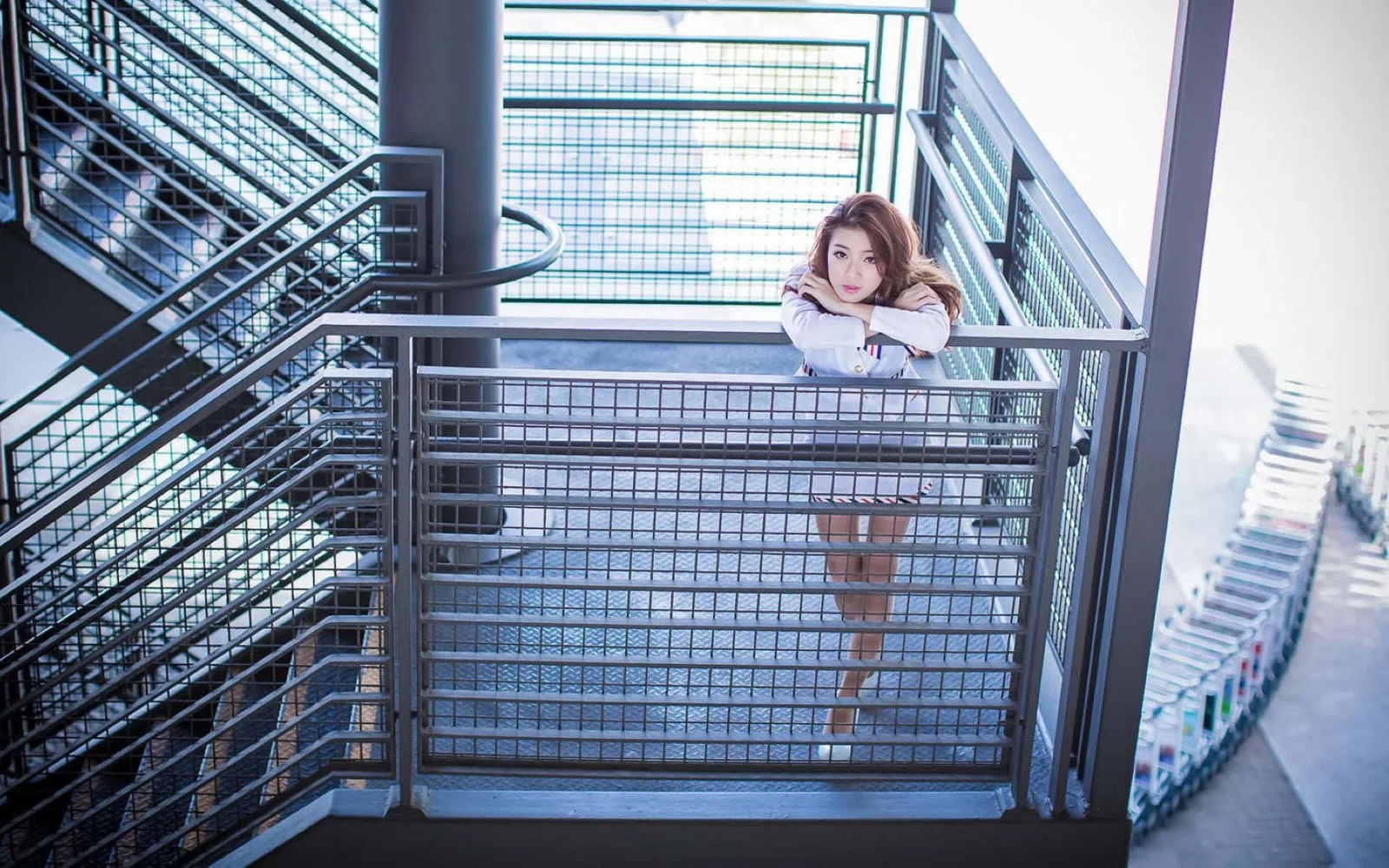 一名成年女性倚靠在现代玻璃钢结构楼梯间的金属栏杆上。