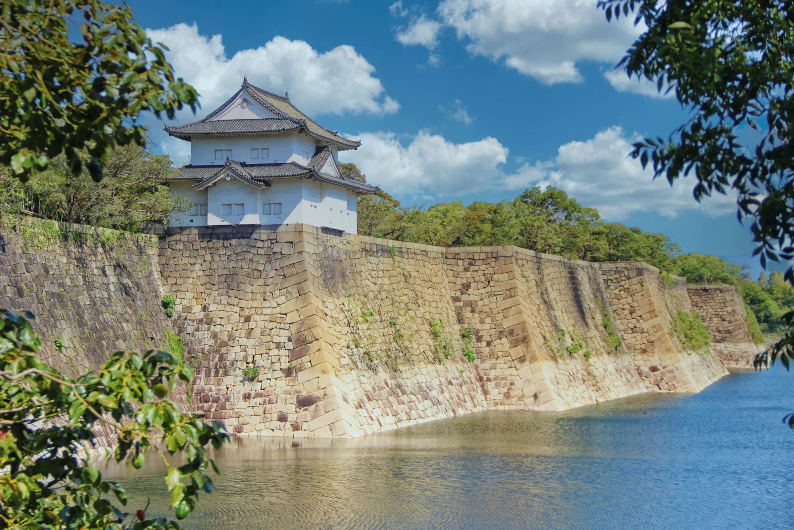 蓝天下，一座白色城堡坐落在石墙和护城河旁，周围环绕着绿树。