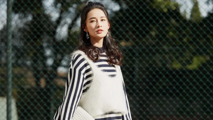 一名成年女性穿着条纹毛衣站在户外的围网前。