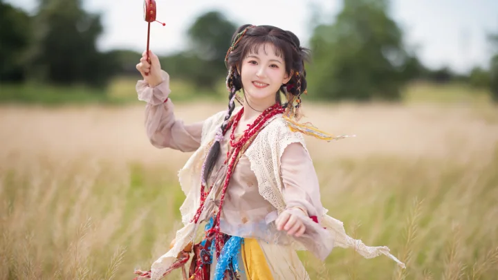 전통 의상을 입은 여성이 들판에 서서 화려한 장식물을 들고 있으며 배경에는 흐릿한 나무와 풀이 보인다.