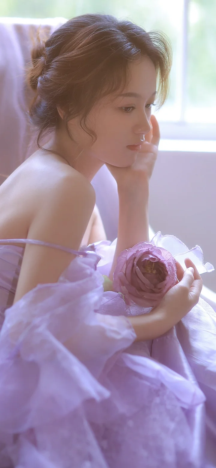 一名身穿淡紫色裙子的女子坐在窗边，手捧一朵紫色玫瑰。