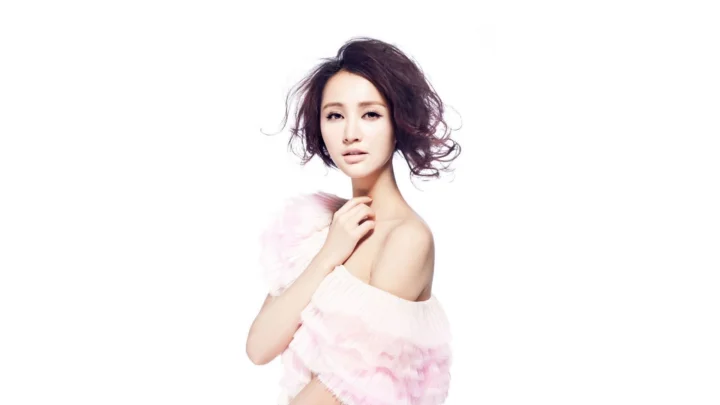 一位成年女性在白色背景前摆姿势，身穿浅粉色露肩上衣。