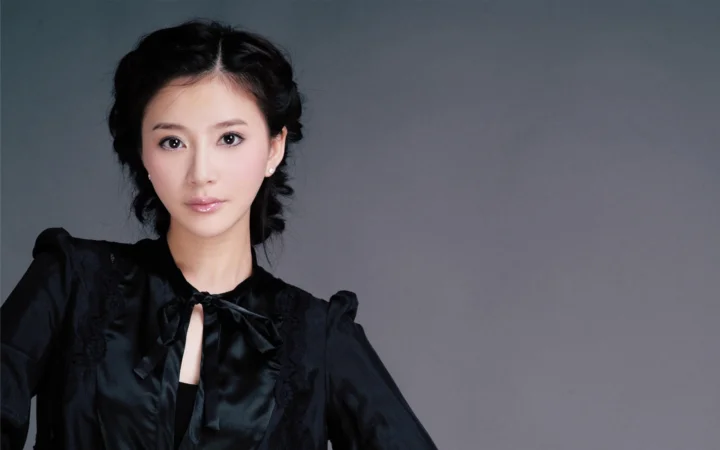 一名成年女子穿着黑色连衣裙，在灰色背景前面对镜头。