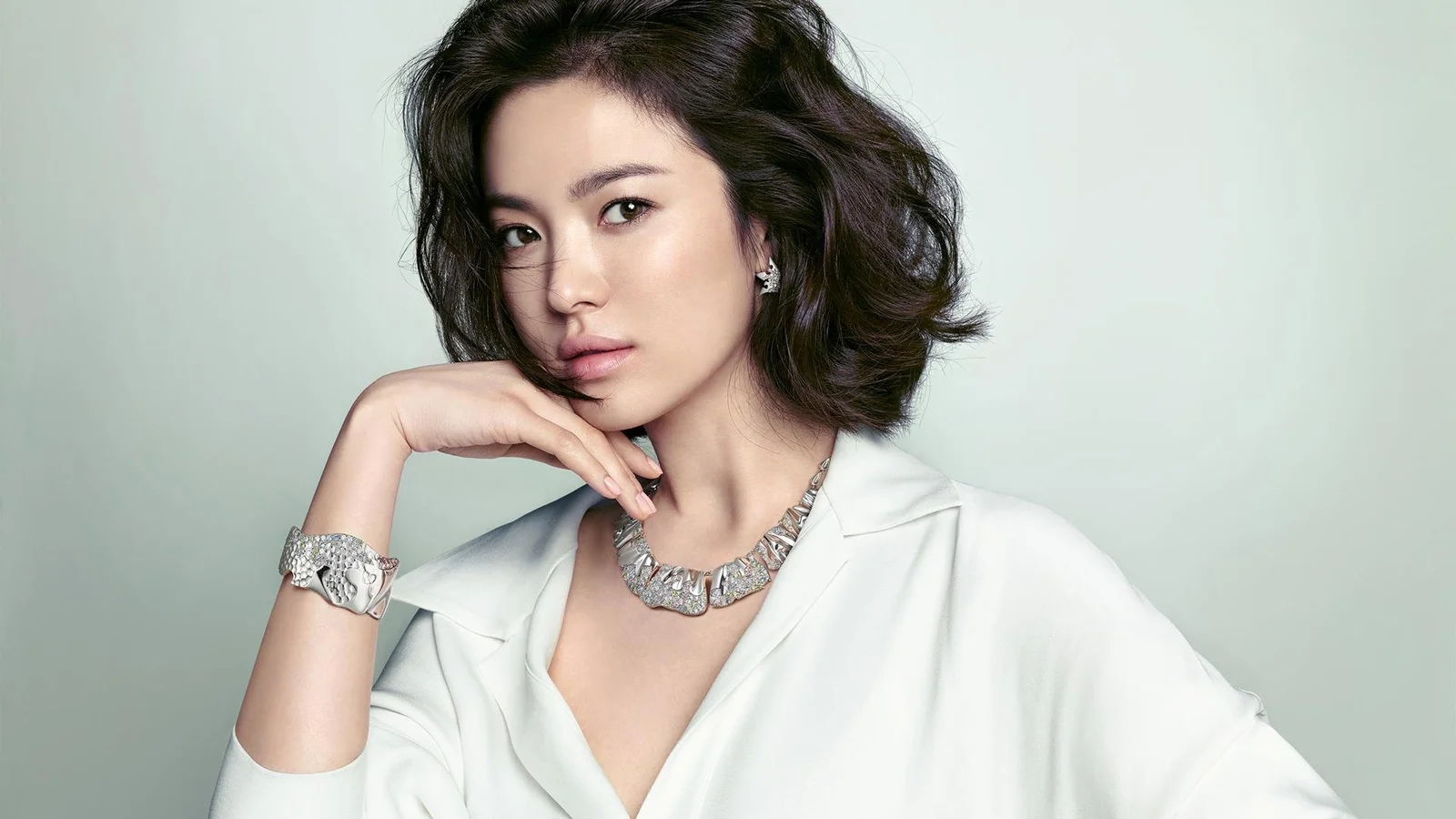 밝은 배경 앞에서 흰 셔츠를 입은 성인 여성이 우아한 포즈를 취하고 있습니다.
