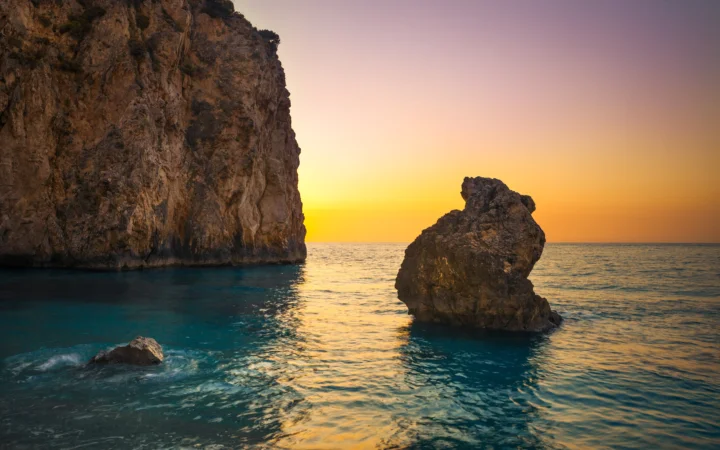 夕阳映照着宁静海面，岩壁与海中巨石构成壮丽的海岸风景。
