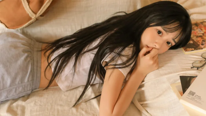 一名长发女性侧卧在床上，手指轻触嘴唇，周围可见书籍和眼镜。