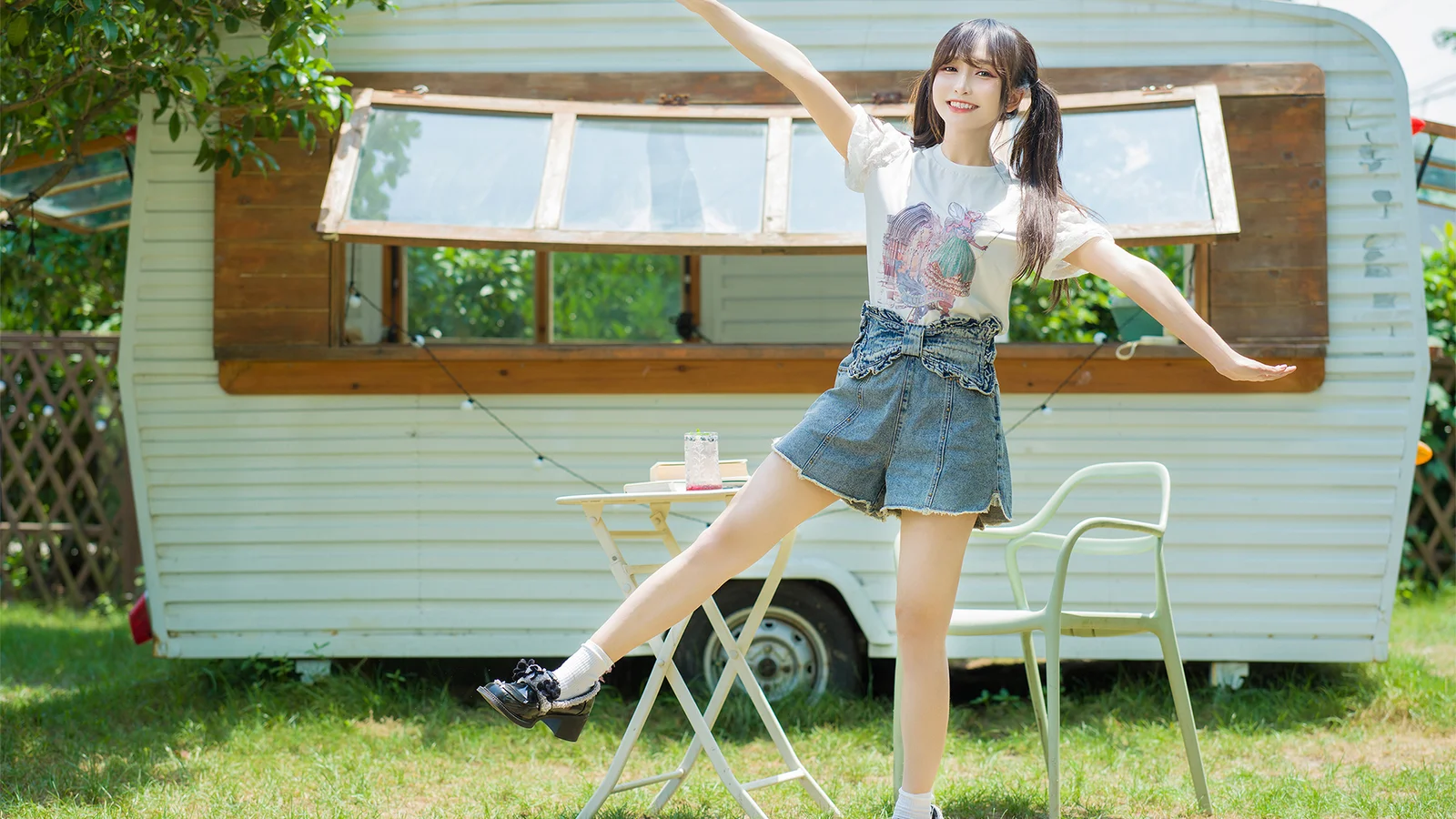一名女子站在草地上的露营车前展开双臂。