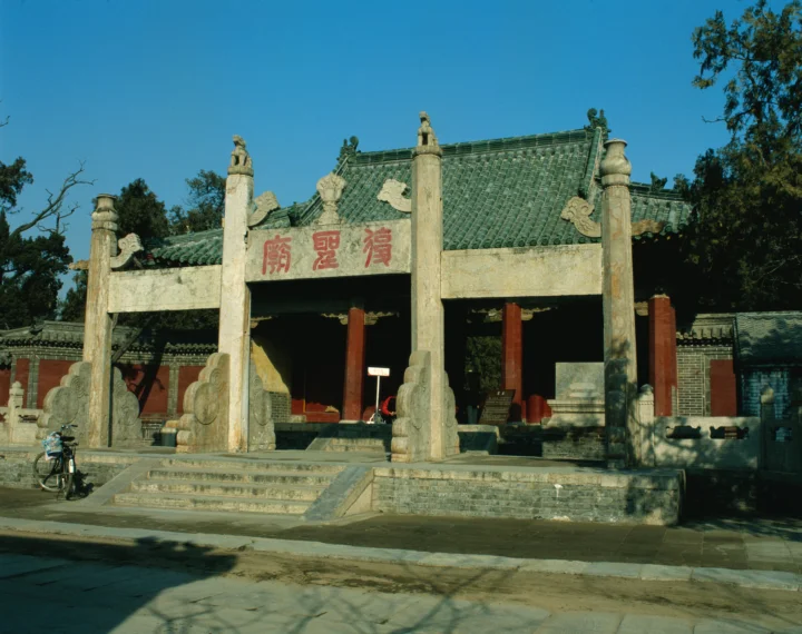 青空の下に立つ古い中国建築の門と、手前の石段や通りが写っています。