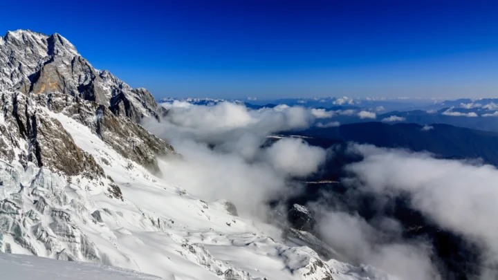 白雪覆盖的高山耸立在云海之上，远处是湛蓝天空与连绵山脉。