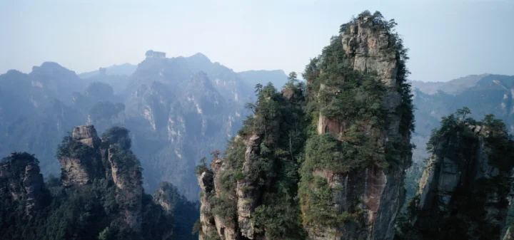 层叠的山峰、岩柱与松林在淡蓝色天空下延伸至远方。