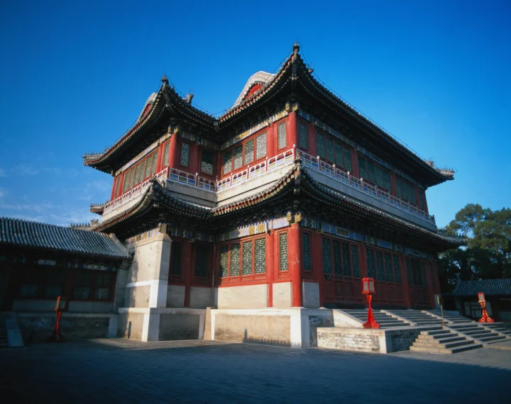 蓝天下，一座红色木构古建筑坐落在石砌庭院中。