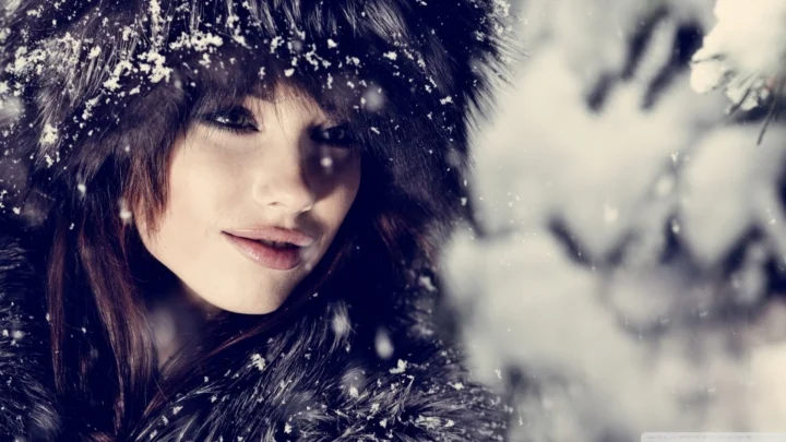 一名成年女子在飘雪中裹着深色毛衣，画面呈现出柔和的冬日氛围。