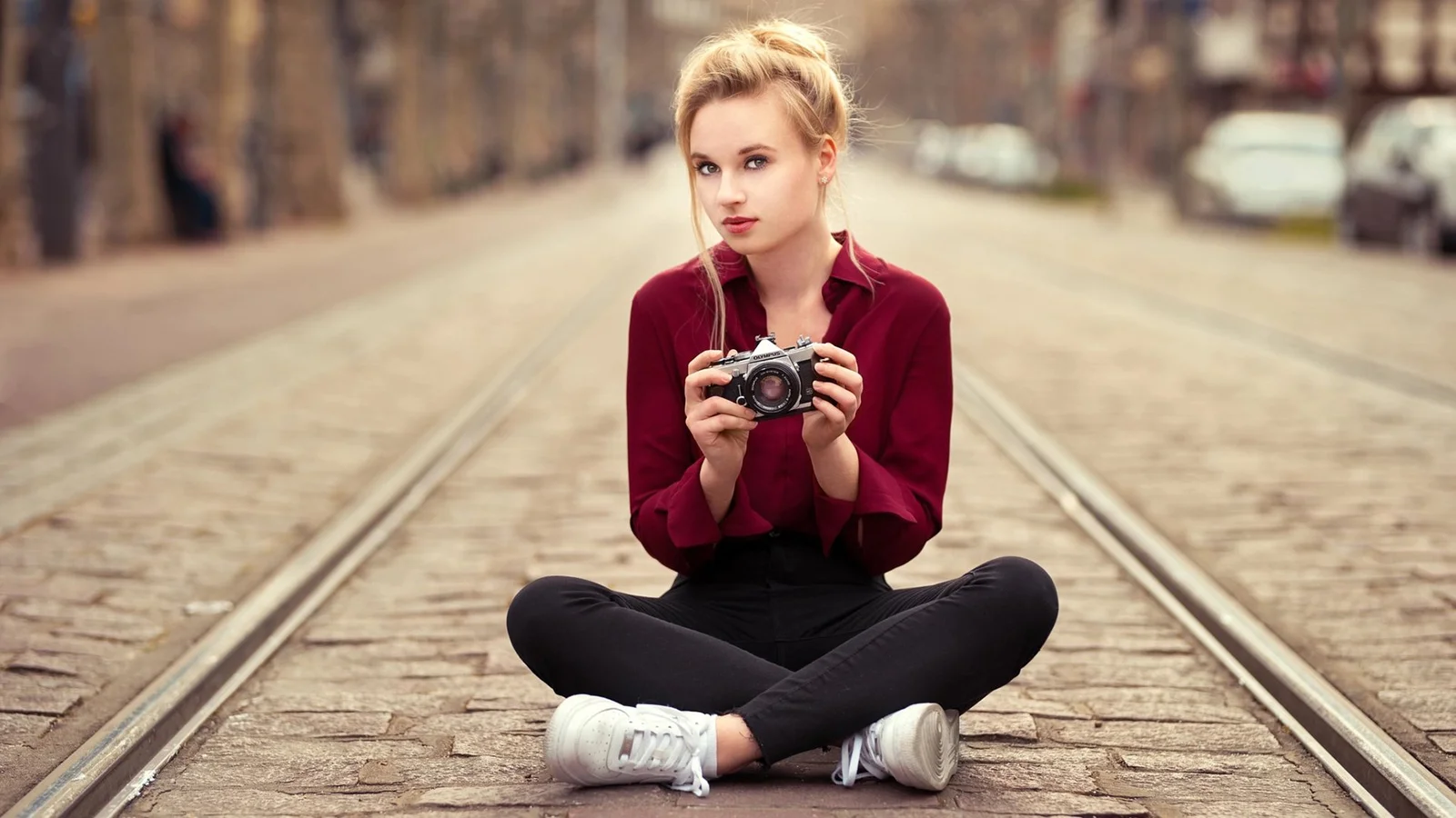 女性が線路の上に座り、カメラを手にこちらを見ている。