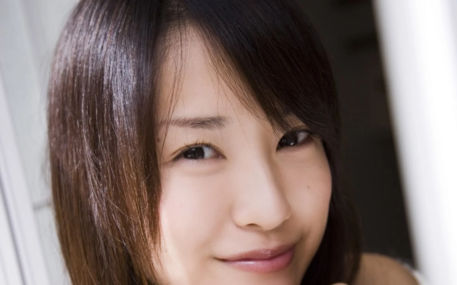 갈색 머리의 여성이 미소를 지으며 카메라를 바라보는 클로즈업 초상입니다.