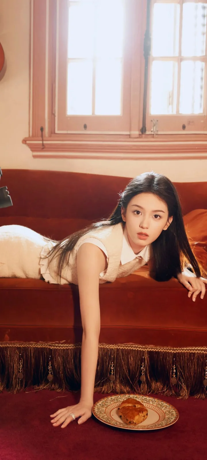 一名女性俯身靠在红色沙发上，窗户透入明亮光线。